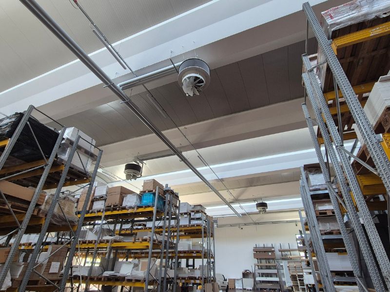 Magazzino industriale con scaffalature metalliche, canalizzazioni a soffitto e diffusori per la ventilazione e la climatizzazione degli ambienti.